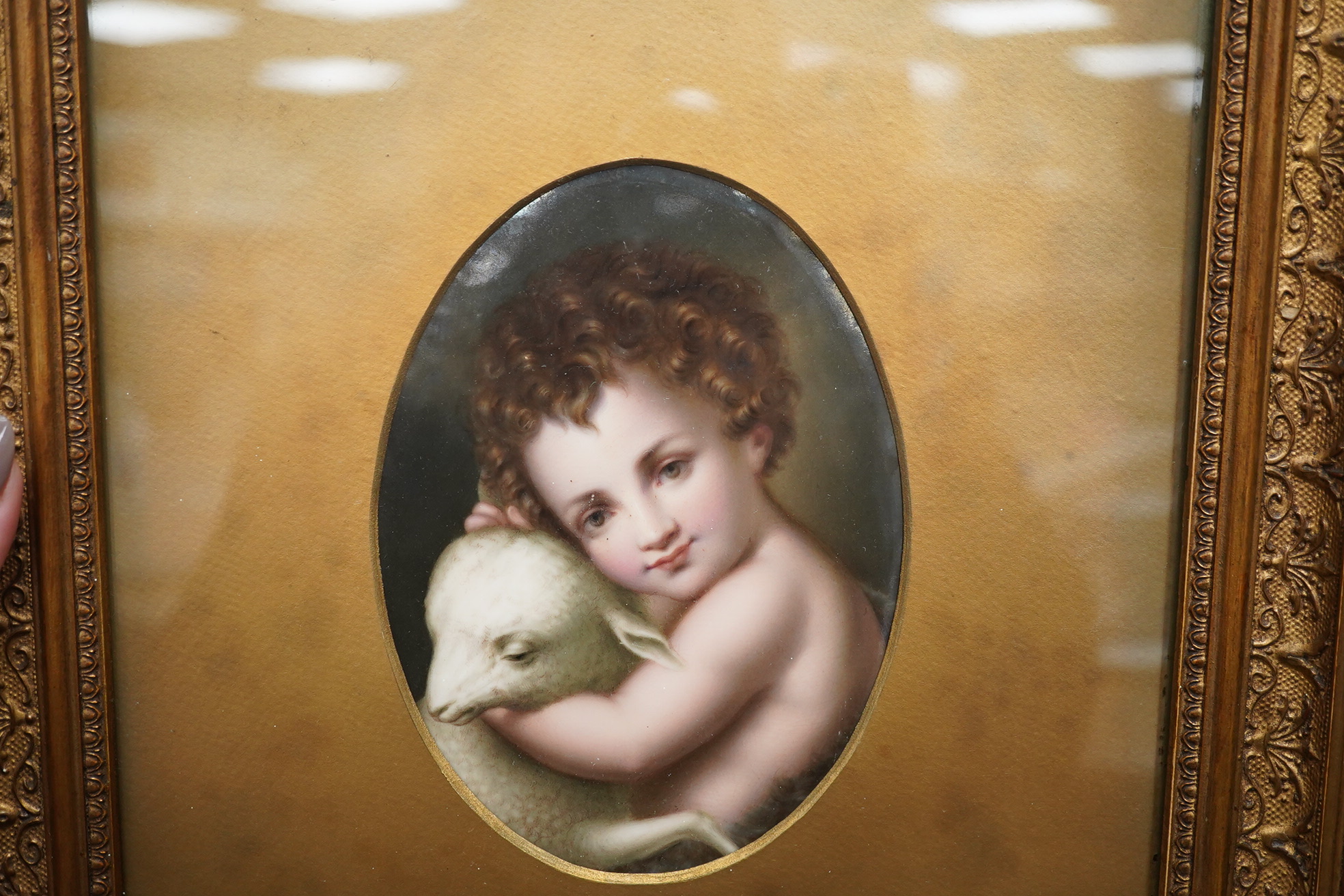 A German oval porcelain plaque with putto and lamb, possibly KPM, ornately gilt framed, overall 39 x 33cm. Condition - fair